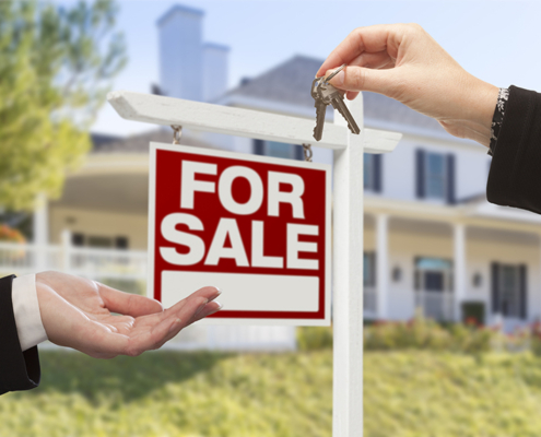 Real Estate Agent Handing Over the House Keys in Front of a Beautiful New Home and For Sale Real Estate Sign.